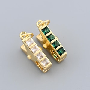 May include: Two gold-colored barrette hair clips. One clip features four clear square-cut stones, and the other has four green square-cut stones. Both clips have a small loop at the top for attaching to hair.