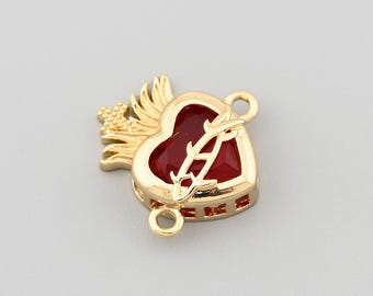 May include: A gold-colored heart-shaped charm with a red center and an arrow piercing through it. The charm has small gold wings on the left side and two loops for attaching to jewelry. The charm is on a plain white background.