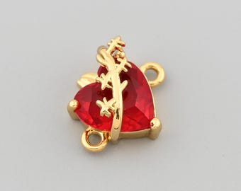 May include: A gold-colored charm with a heart-shaped, faceted red gemstone. The charm has a decorative gold accent and two small loops for attachment. The heart measures approximately 0.5 inches in width.