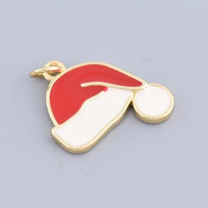 Puede incluir: Un dije dorado con forma de gorro de Papá Noel. El gorro tiene una corona roja, un borde blanco y un pompón blanco. Un accesorio festivo para la temporada navideña.