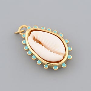 May include: Gold-toned pendant featuring a cream-colored seashell encased in a gold frame with turquoise accents. The pendant has a small loop for attaching to a chain or other jewelry. The design is oval-shaped.