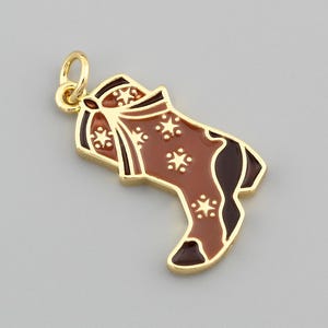 May include: A gold-colored Christmas stocking pendant with a brown and dark brown enamel design. The stocking features white snowflake accents and a bow at the top. The pendant is a festive holiday accessory.