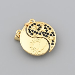 May include: A gold-coloured pendant featuring a Yin and Yang design. One half of the pendant depicts a sun with rays, while the other half is adorned with black gemstones. The pendant has a loop for a chain.