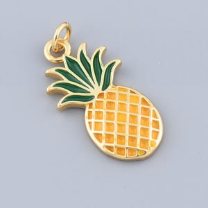 May include: A gold-colored pineapple charm with green leaves and a yellow body. The charm has a small loop at the top for attaching to a necklace or bracelet. The pineapple design is detailed with a grid pattern.