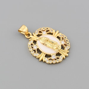 May include: Gold-tone pendant featuring a religious figure within a white oval, surrounded by clear crystals and ornate gold detailing. The pendant has a bail for attaching to a chain and is set against a gray background.