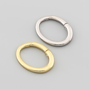 Puede incluir: Dos cierres metálicos de forma ovalada, uno dorado y otro plateado. Cada cierre tiene un diseño con bisagras para abrir y cerrar. Los cierres se muestran sobre un fondo gris claro. Adecuado para la fabricación de joyas.