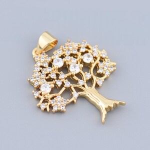 May include: A gold-colored tree pendant with clear, sparkling crystals. The pendant features a detailed tree design with a trunk, branches, and crystal-studded leaves. The pendant has a loop for a chain.