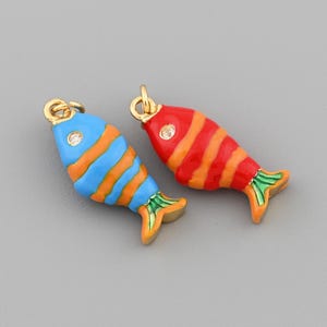 May include: Two colorful fish-shaped charms. One is blue with orange stripes, the other is red with orange stripes. Both have gold-colored accents and a small gem. The charms are likely for jewelry making.