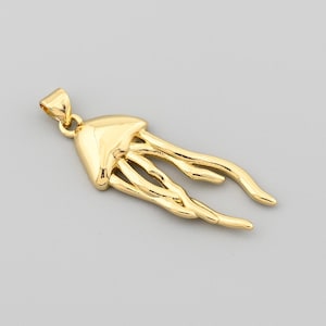 May include: A gold-colored pendant in the shape of a jellyfish. The pendant has a rounded bell and flowing tentacles. The bail is a simple loop for attaching to a chain. The jellyfish design is detailed and shiny.