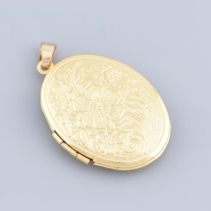 May include: A gold-colored oval locket with a floral design. The locket has a hinged opening and a small loop for a chain. The surface is embossed with a detailed pattern of flowers and leaves.