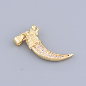 May include: A gold-colored pendant in the shape of a curved claw, adorned with small, clear gemstones. The top of the pendant features a detailed carving of a wolf's head. The pendant is designed to be worn as a necklace.