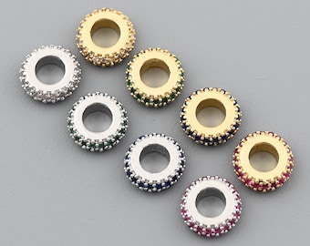 May include: An assortment of small, circular beads. Each bead features a central hole surrounded by a ring of small, colorful gemstones. The beads are in various colors, including gold, silver, green, blue, and red.