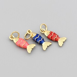 May include: Three colorful fish charms with gold-colored accents. The fish are in shades of red, blue, and pink, with gold-colored fins and a loop for attaching to a chain or bracelet. The charms are set against a gray background.