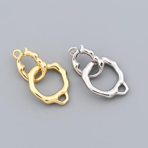 May include: Two metal jewelry clasps. One is gold-colored, the other is silver-colored. Both clasps have an organic, irregular shape with a loop and a clasp mechanism. The clasps are designed for jewelry making and crafting.