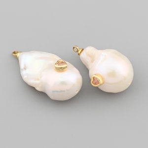 May include: Two baroque pearl pendants with gold-colored accents and small pink gemstones. The pearls are white with a lustrous sheen. The pendants are displayed against a gray background.
