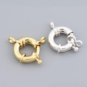 May include: Two round jewelry clasps, one gold-toned and one silver-toned, are displayed against a gray background. The clasps have a circular design with a spring-loaded mechanism for secure closure. These clasps are ideal for necklaces and bracelets.