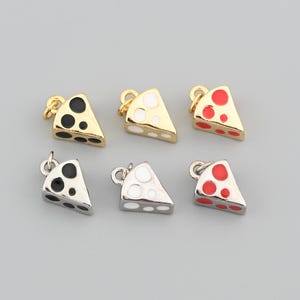 Peut inclure: Six petits charms en forme de part de fromage, en tons or et argent. Chaque charm a une boucle pour l'attacher à un bijou. Les tranches de fromage ont des accents de points noirs, blancs et rouges. Les charms sont disposés sur un fond gris clair.