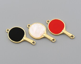 Pode incluir: Três pingentes dourados em forma de raquete de pingue-pongue com faces de cores diferentes: preto, branco e vermelho. Cada pingente tem uma argola na parte superior para prender a joias ou outros trabalhos manuais. As raquetes estão dispostas sobre um fundo cinza.