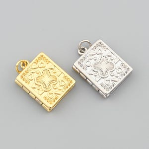 May include: Two rectangular pendants, one gold and one silver, with a hinged design. Each pendant features an ornate, symmetrical pattern of hearts and a central four-leaf clover design. The pendants have a small loop at the top for attaching to a chain.