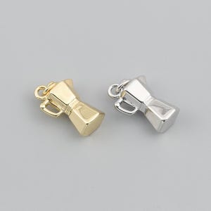 May include: Two small metal charms shaped like moka pot coffee makers. One charm is finished in a polished gold tone, while the other is finished in a polished silver tone. Each charm features a small loop at the top for attachment purposes.