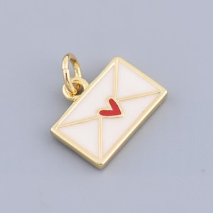 May include: A gold-colored charm in the shape of an envelope with a white enamel front and a red heart. The charm has a small loop for attaching to a necklace or bracelet. The background is a solid gray.
