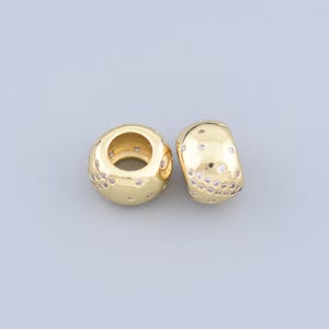 May include: Two gold-colored beads with a polished finish. Each bead is adorned with small, clear, sparkling accents. One bead is round, and the other is a barrel shape. These beads are suitable for jewelry making.