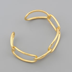 Könnte beinhalten: Ein goldfarbenes Armreif-Armband mit einem Kettenglied-Design. Das Armband hat ein offenes Design und besteht aus einem glänzenden, metallischen Material. Die Glieder sind länglich und durchgehend verbunden.