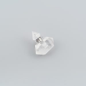 Può includere: Un ciondolo a forma di boccetta di profumo in cristallo trasparente sfaccettato con tappo a punta e un collare in metallo color argento dotato di due piccoli anelli laterali per l'aggancio. La boccetta ha una forma geometrica multifaccettata.