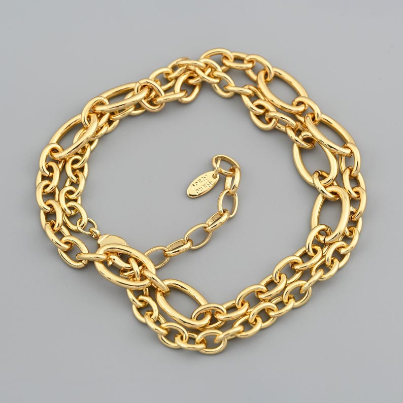 Puede incluir: Un collar dorado con un dise&ntilde;o de cadena de doble hebra. El collar presenta eslabones de forma ovalada y un cierre de mosquet&oacute;n. El collar tiene una peque&ntilde;a etiqueta con texto.