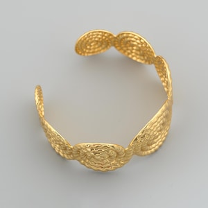 May include: Gold-toned cuff bracelet featuring a textured, hammered design. The bracelet has a series of circular, spiral-like embellishments. The open design allows for easy wear. A stylish piece of jewelry.