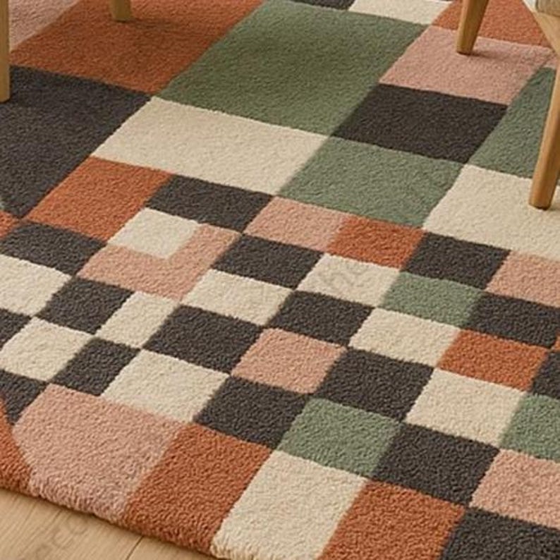 May include: A geometric patterned rug featuring squares in shades of orange, green, pink, cream, and gray. The rug has a textured surface and is partially visible with wooden chair legs in the corners.