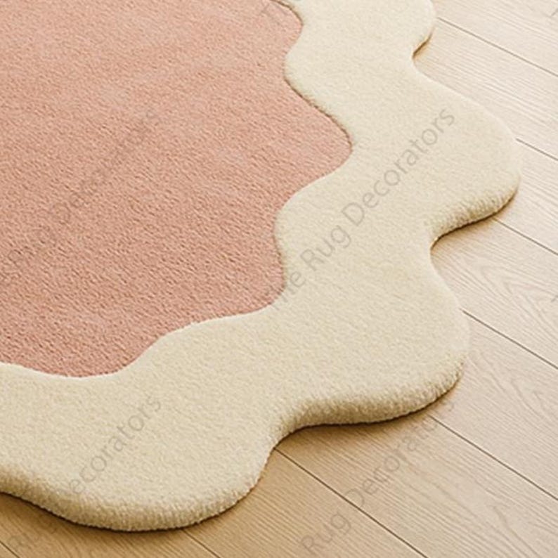 May include: A soft, scalloped rug with a light pink centre and a cream-coloured border. The rug's unique shape and colour palette create a cosy and inviting aesthetic, suitable for various interior styles.