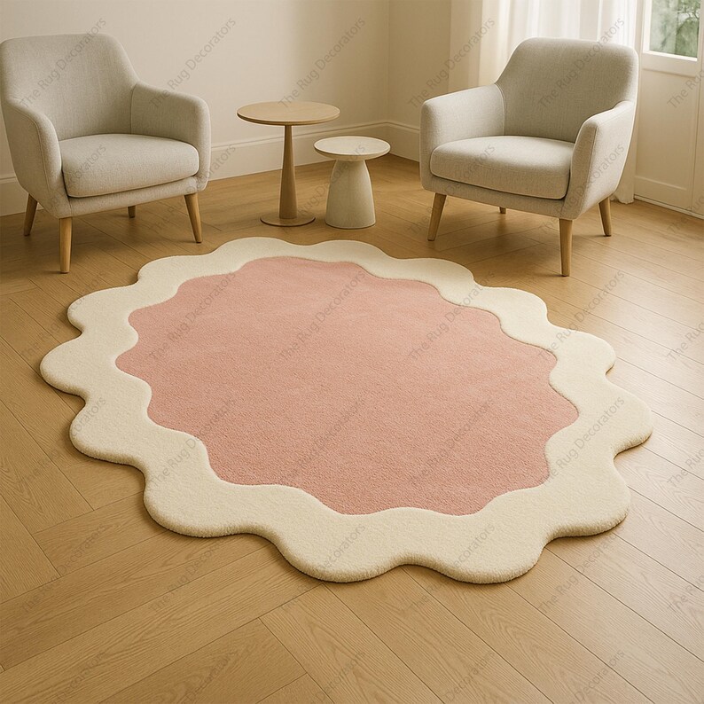 May include: A pink and cream-coloured rug with a distinctive, wavy edge design. The rug is oval-shaped and placed on a light-coloured wooden floor. Two armchairs and small side tables are in the background, creating a cosy interior setting.