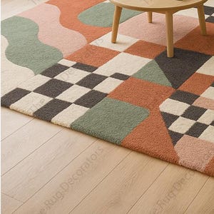May include: A colorful area rug with a geometric pattern. The rug features squares, triangles, and organic shapes in shades of orange, pink, green, and gray. A small wooden table with a round top and four legs sits on the rug.