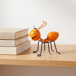 Peut inclure: Une figurine de fourmi en métal décorative avec une tête et un abdomen orange vif parsemés de taches noires, de grands yeux blancs à pupilles noires, deux antennes orange et six fines pattes en fil noir reliées par un ressort central.