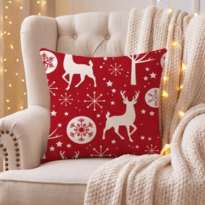 Könnte beinhalten: Ein quadratisches Dekokissen mit einem leuchtend roten Hintergrund und einem sich wiederholenden weißen Muster aus Rentieren, verschiedenen Schneeflockenmotiven, kleinen Sternen und stilisierten Baum-Silhouetten auf der gesamten Stoffoberfläche.