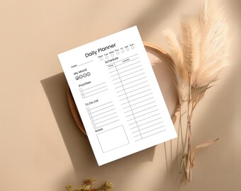 Puede incluir: Una hoja blanca de "Daily Planner" con texto negro, que incluye secciones para la fecha, el estado de ánimo, las prioridades y una lista de tareas. El planificador está sobre una bandeja de madera con plantas secas decorativas.