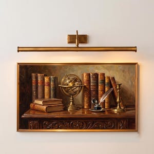 May include: A rectangular wall-mounted brass picture light fixture positioned above a framed oil painting. The painting depicts a dark wooden desk with several leather-bound books, a brass armillary sphere, an inkwell with a quill, and a candlestick.