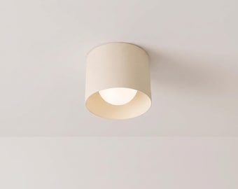 May include: A cylindrical ceiling light fixture with a matte cream finish. The fixture features a wide, open bottom design that reveals a glowing, spherical white light bulb centered within the housing. The text MATTE CREAM FINISH is visible.