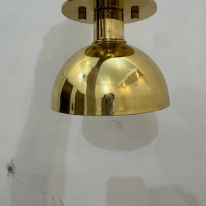 Op de afbeelding: Een vintage messing hanglamp. De lamp heeft een afgeronde, koepelvormige kap en een cirkelvormige bovenkant. De lamp hangt aan een messing staaf. De gepolijste messing afwerking geeft het licht een warme gloed. Ontworpen voor plafondmontage.