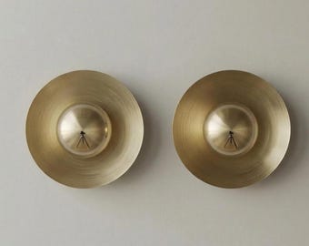 May include: Two brass-colored wall sconces. Each sconce has a circular, disc-shaped base with a central, spherical light fixture. The light fixtures have a small, tripod-like detail. The sconces are mounted on a light gray wall.