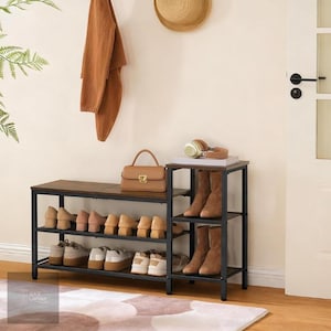 May include: A brown and black shoe rack with a bench seat, featuring three shelves for shoes and a side section for boots. A brown handbag and headphones sit on top. A brown coat and straw hat hang on the wall.