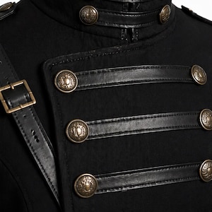 May include: Black military-style jacket with a high collar and decorative gold-colored buttons. The jacket features leather accents and a shoulder strap with a buckle. The design is reminiscent of historical military uniforms.