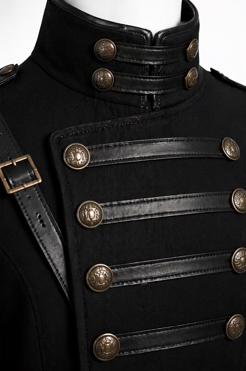 May include: Black military-style jacket with a high collar and decorative gold-colored buttons. The jacket features leather accents and a shoulder strap with a buckle. The design is reminiscent of historical military uniforms.