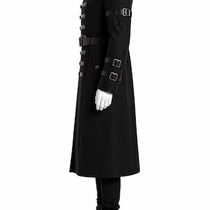 May include: Black military-style coat with multiple button closures, a high collar, and leather accents. The coat features a belt at the waist and straps on the sleeves. The model is wearing black pants and boots.