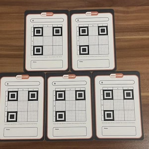 Könnte beinhalten: Fünf weiße Karten mit schwarzem Rand und dem Text "SEED SIGNER" oben. Jede Karte hat ein Raster, drei schwarze Quadrate und einen Platz für Notizen. Die Karten sind auf einer Holzoberfläche angeordnet.