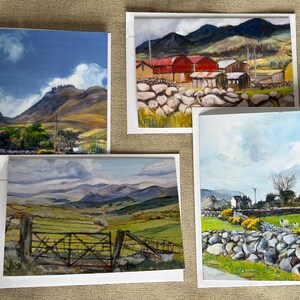 以下が含まれることがあります： 山、畑、田舎の建物など、風景画の4つのアートプリント。絵画は、青、緑、茶色など様々な色を使用し、石壁や門があります。プリントはニュートラルな背景に表示されています。