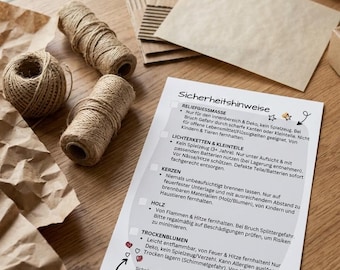 May include: A still-life shot featuring craft supplies on a wooden surface. The image includes spools of twine, crumpled brown paper, cardboard pieces, and a white card with German text about safety precautions.