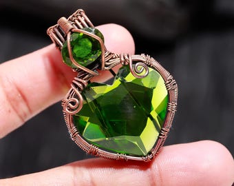May include: A handcrafted pendant featuring a heart-shaped, faceted green gemstone. The gemstone is encased in copper wire, with a smaller green stone above. The wirework includes decorative swirls and a bail for a chain.