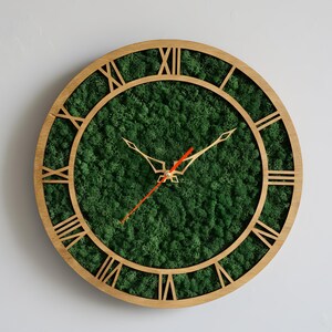 May include: Round wooden wall clock with a natural moss green face and gold-colored hands. The clock features Roman numerals and a red second hand, creating a unique and decorative timepiece for home decor.